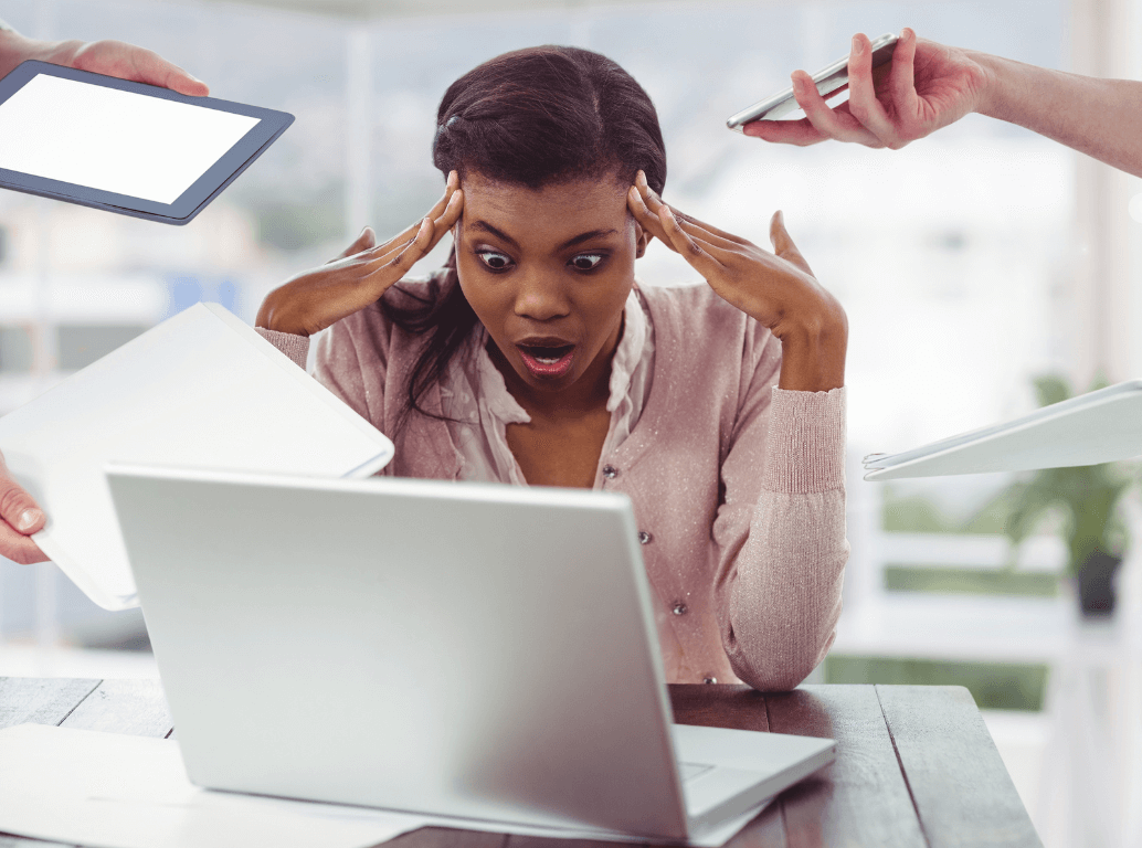 Shocked employee overwhelmed by work at laptop while colleagues hand her multiple tasks, showing the true cost of a bad hire in business